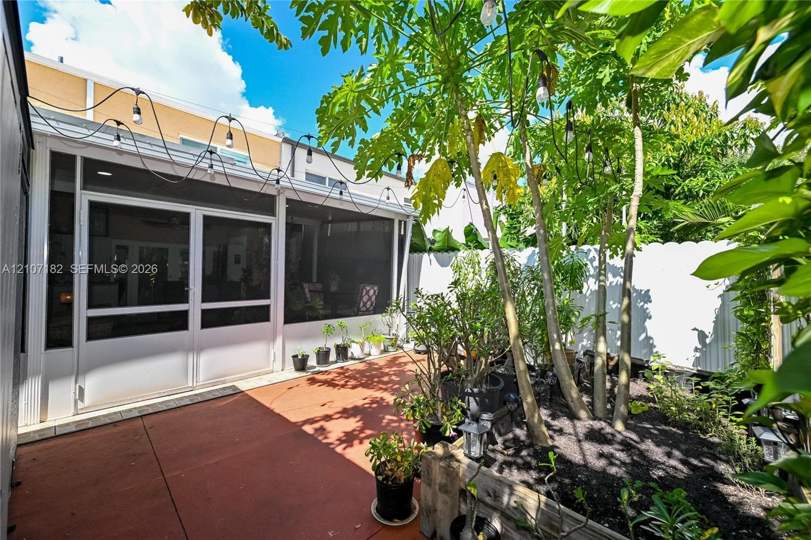 Screened-in patio with hardscaped flooring, white perimeter fencing, and integrated overhead string lighting