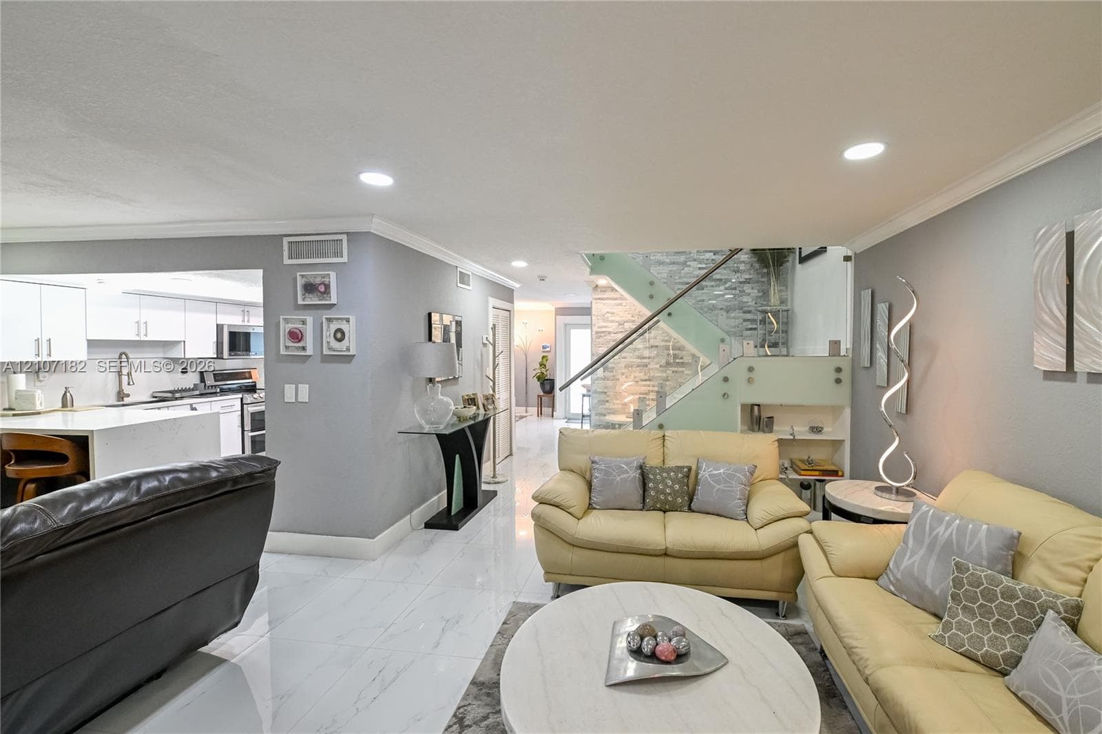 Interior featuring large-format tile flooring, recessed lighting, and a staircase with glass panel railing and stone-textured accent wall