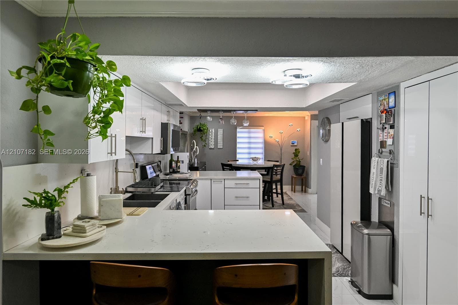 Kitchen featuring white high-gloss cabinetry, stone-finish countertops, dual-basin undermount sink with goose-neck faucet, recessed tray ceiling lighting, and floor-to-ceiling built-in pantry storage