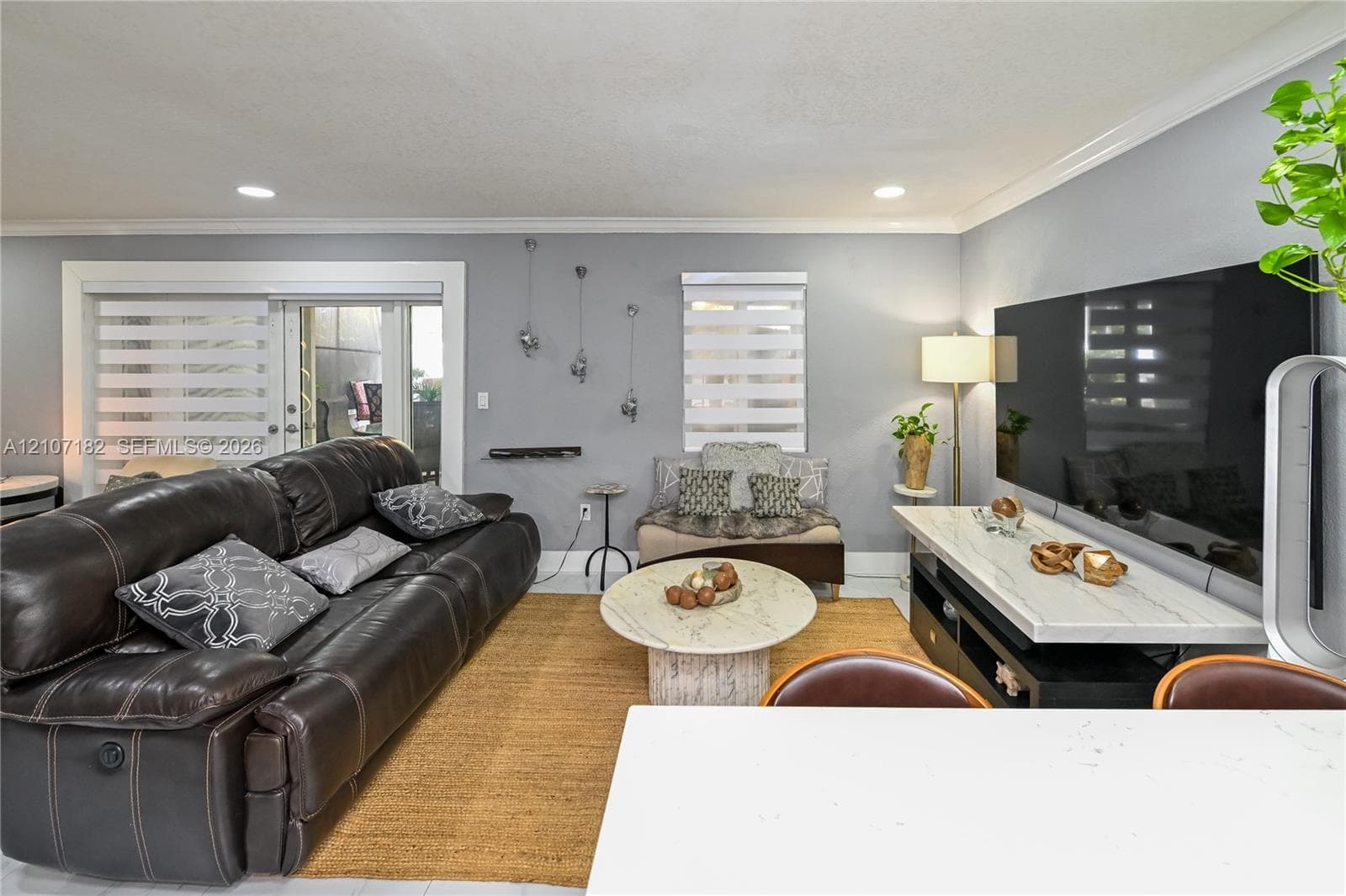 Living area featuring crown molding, recessed lighting, neutral wall paint, and sliding glass doors with roller shades