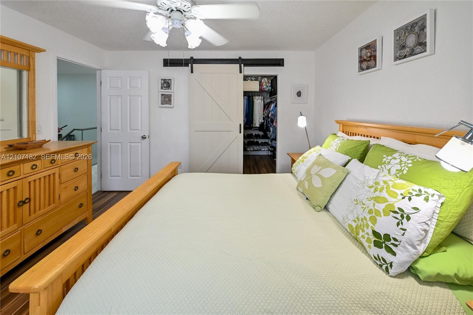 Sliding barn-style door, wood-finish flooring, ceiling fan with multi-light fixture, and six-panel interior door
