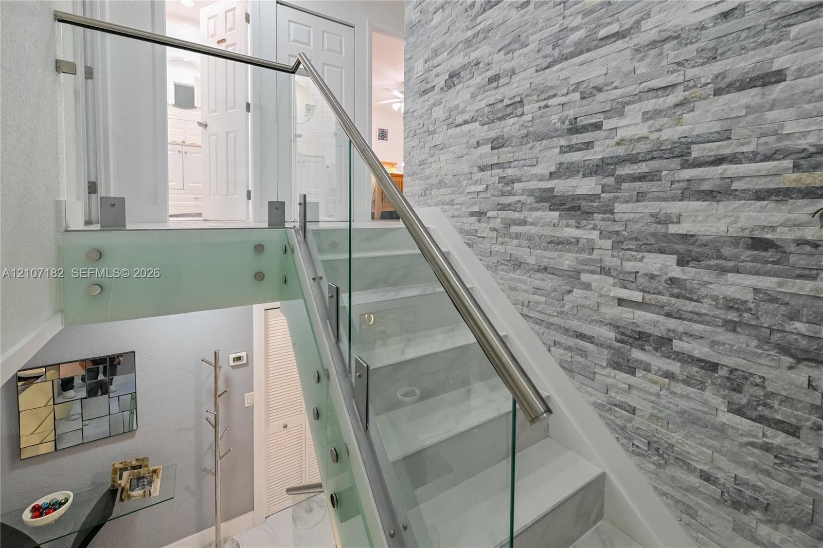 Staircase featuring stacked stone accent wall, glass panel railings, metal handrails, and solid-surface treads