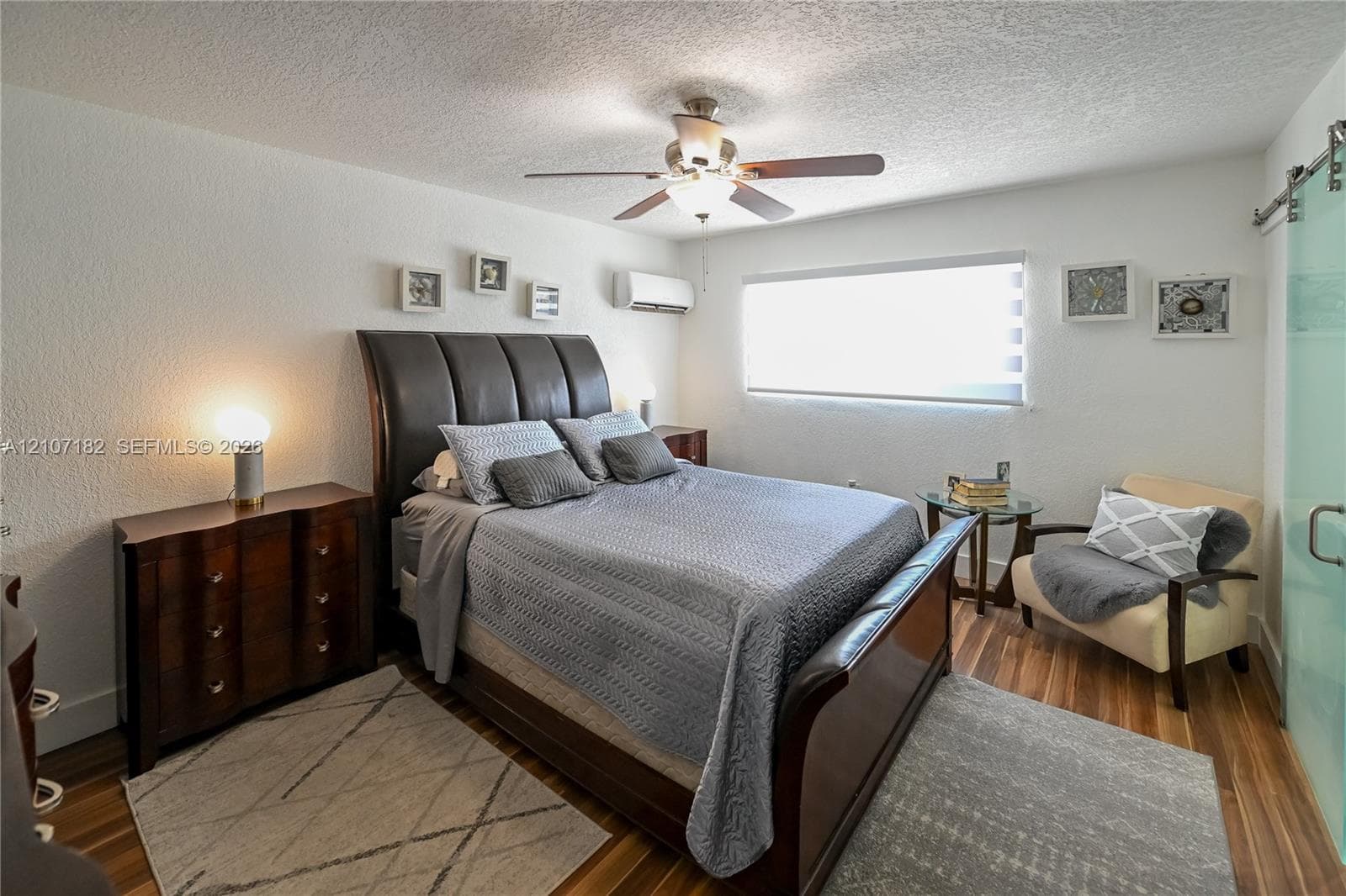 Room featuring wood-finish flooring, a ceiling fan with integrated lighting, wall-mounted climate control unit, and a sliding glass door with a metal track system
