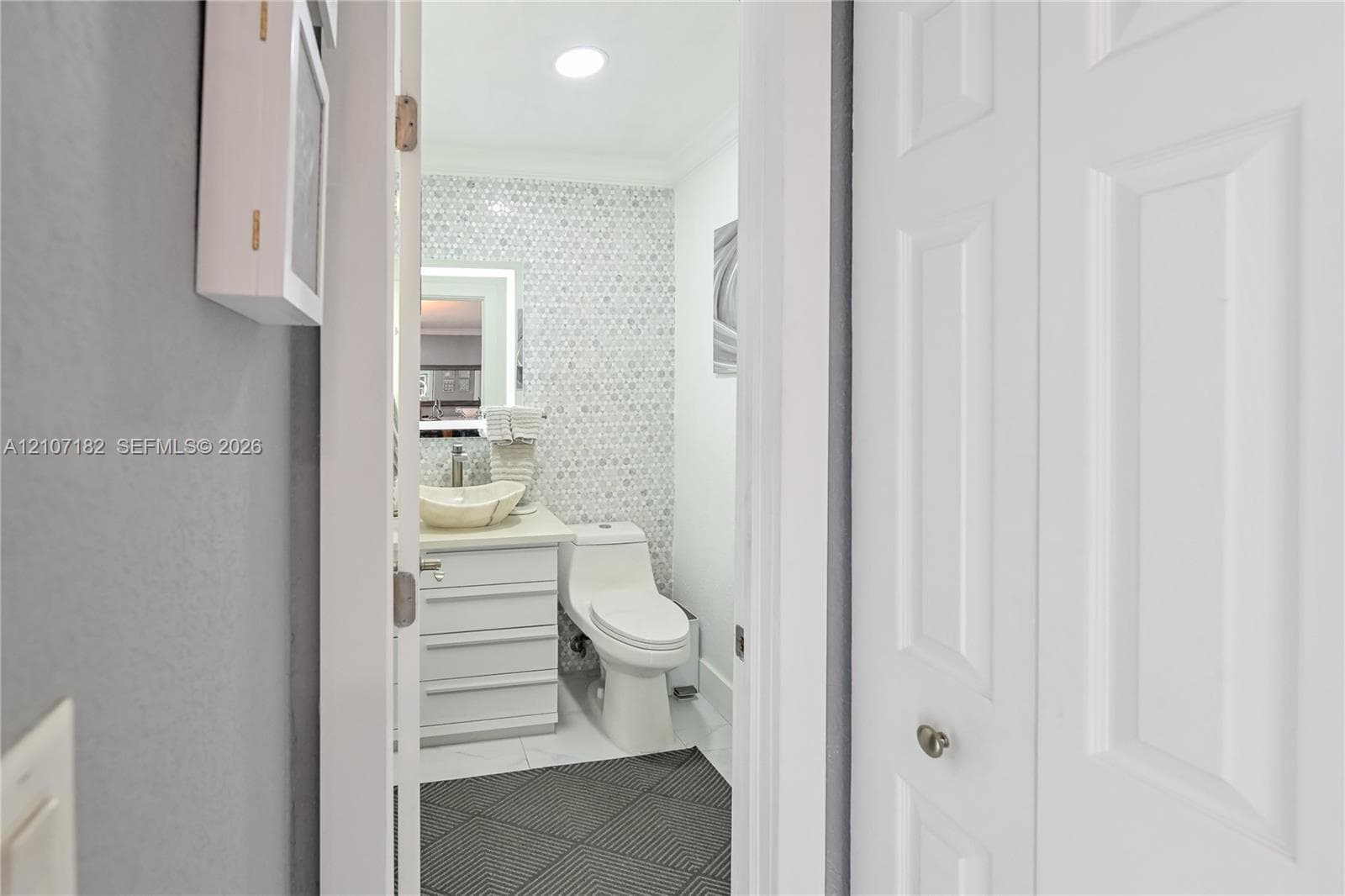 Bathroom featuring a white vanity cabinet with a vessel sink, geometric mosaic tile wall, one-piece dual-flush toilet, and diamond-patterned floor tile