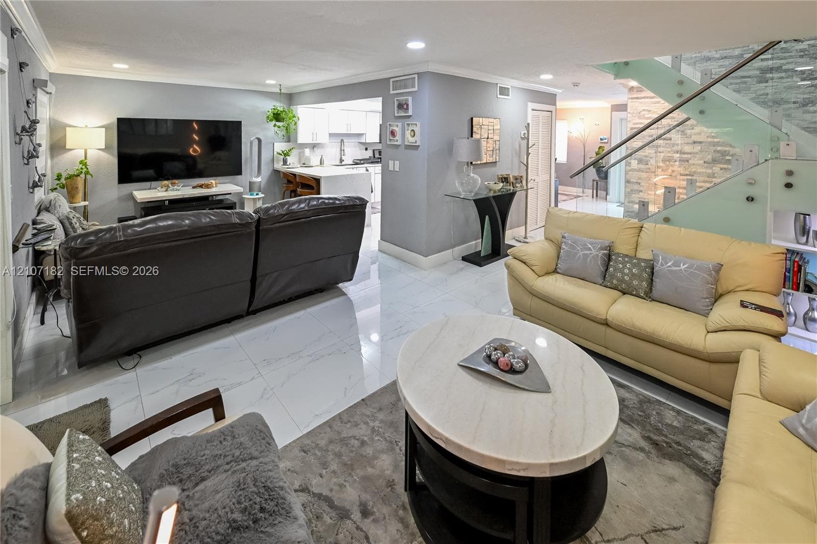 Large-format tile flooring, staircase with glass paneling and stainless steel railings, stone-accented wall, and recessed ceiling lighting