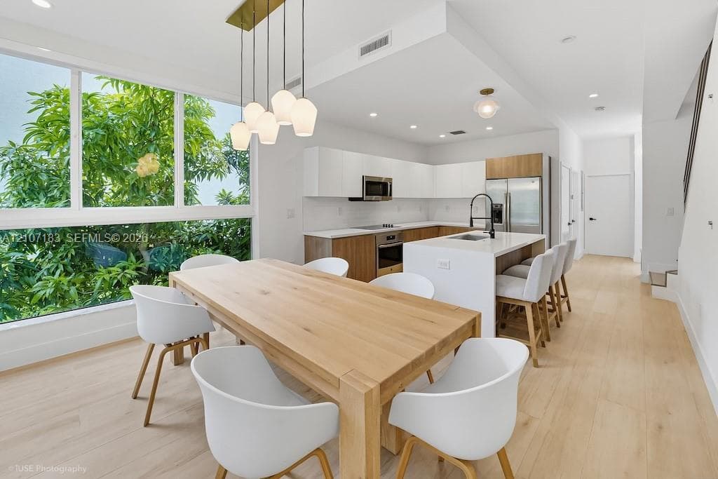 Kitchen featuring two-tone flat-panel cabinetry, a central island with a quartz countertop, wood-finish flooring, floor-to-ceiling windows, and contemporary multi-pendant lighting