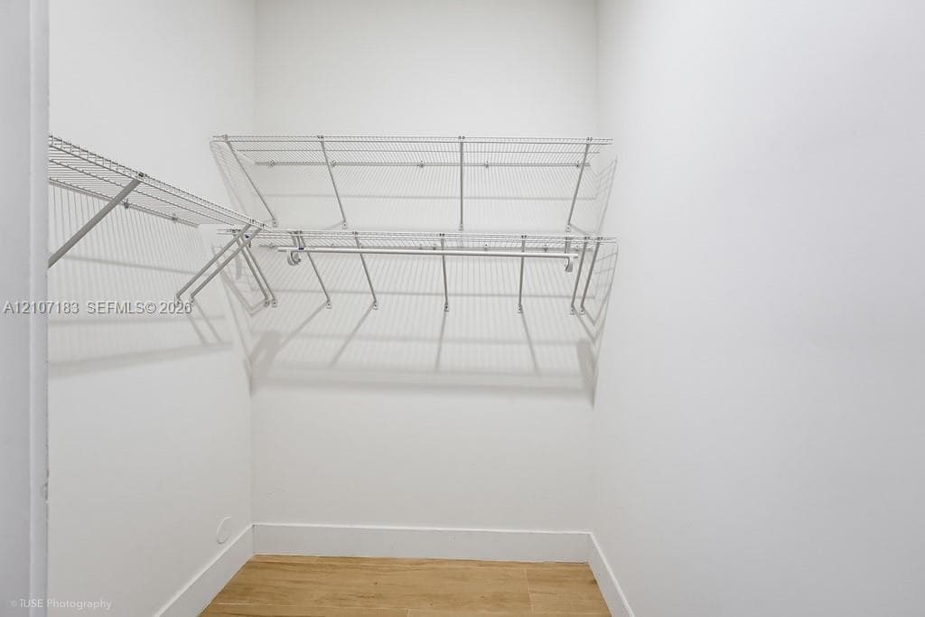 Walk-in storage space featuring multi-tiered white wire shelving, integrated hanging rods, and wood-finish flooring