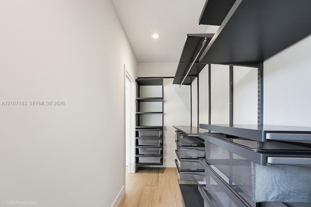 Custom storage system featuring matte black metal shelving, integrated pull-out wire baskets, hanging rods, and wood-finish flooring