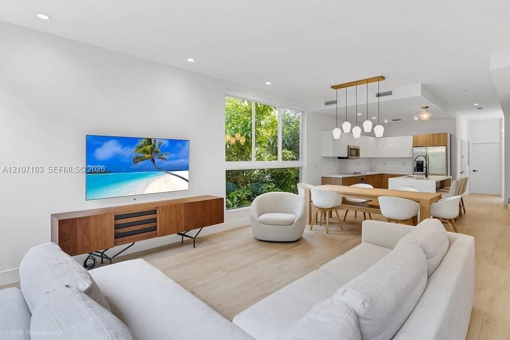 Open-concept living space featuring wood-finish flooring, recessed lighting, multi-pane floor-to-ceiling windows, and a kitchen equipped with cabinetry and a center island