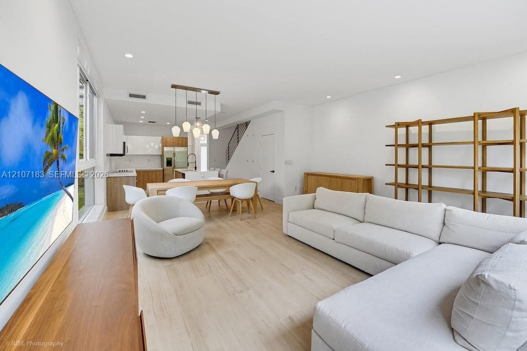 Open-concept living space featuring wood-finish flooring, recessed lighting, and a modern kitchen with flat-panel cabinetry and a multi-pendant light fixture