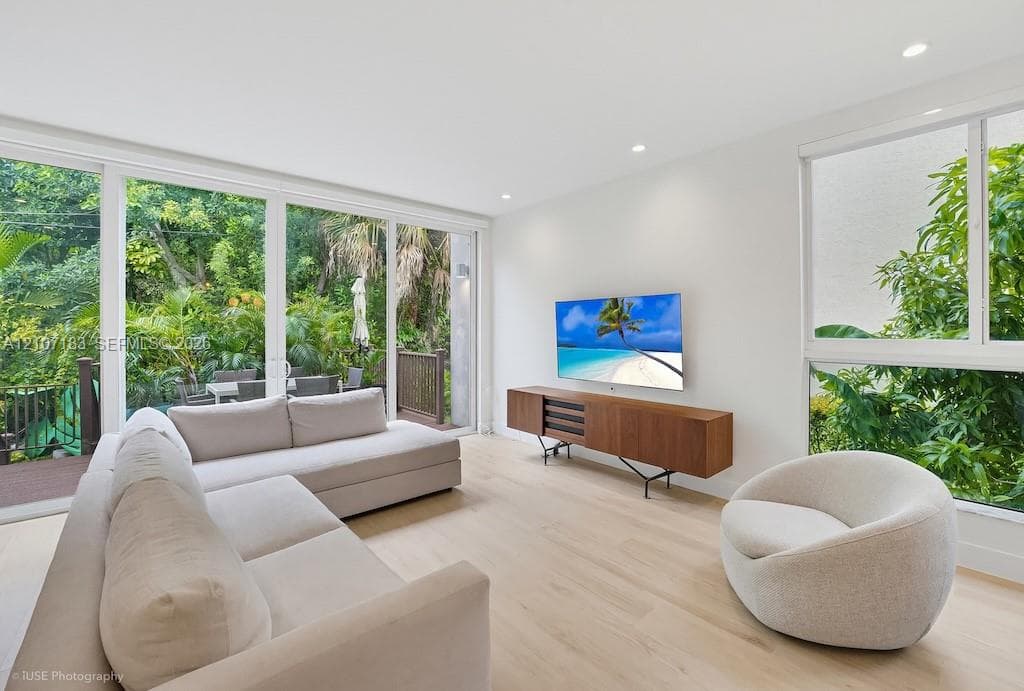 Floor-to-ceiling glass sliding doors, wood-finish flooring, recessed lighting, and large windows with greenery exposure
