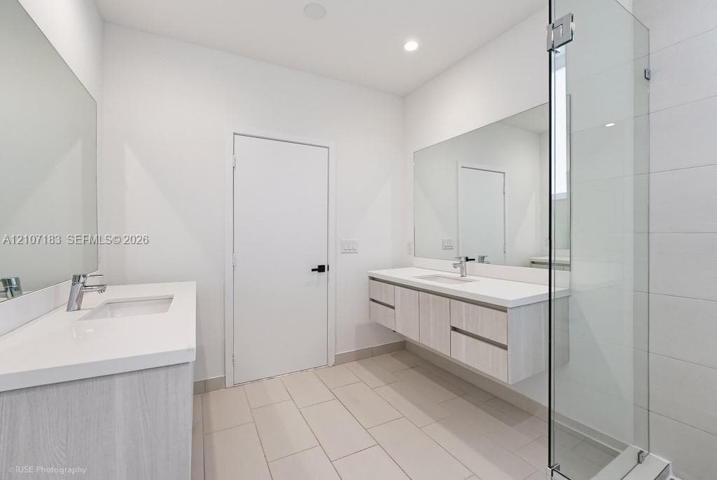 Floating dual vanities with white countertops and undermount sinks, full-width wall mirrors, large-format tile flooring, and a walk-in glass-enclosed shower