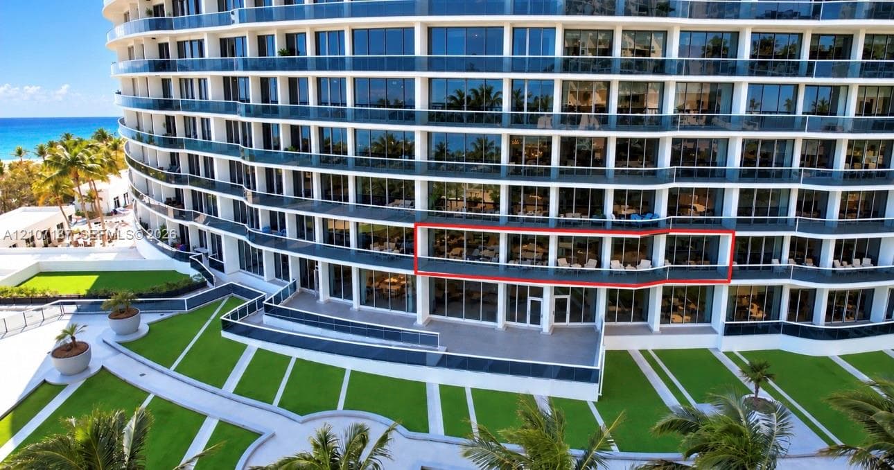 Multi-story glass-facade residential building featuring expansive private balconies, floor-to-ceiling windows, and manicured landscaping