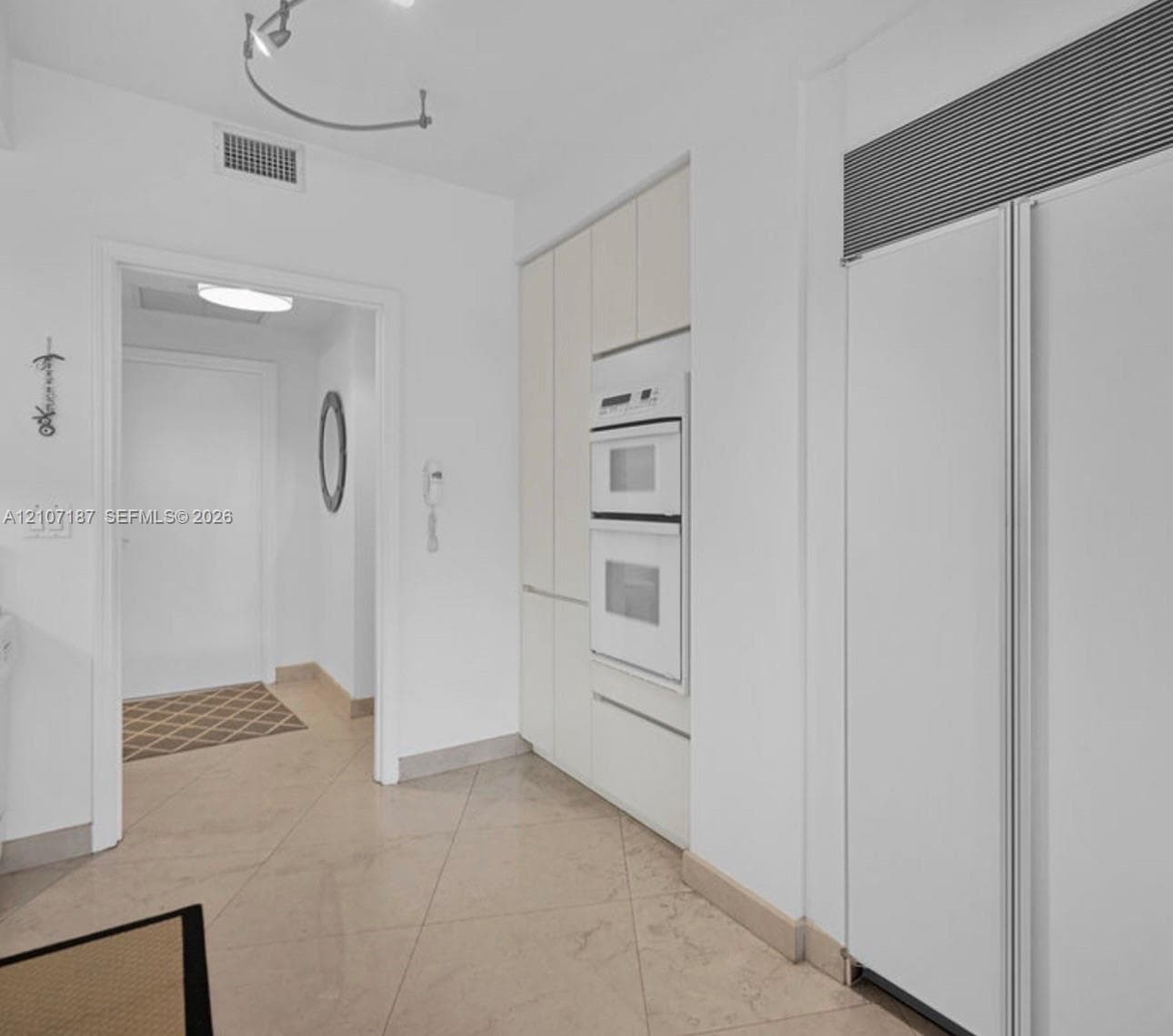 Built-in floor-to-ceiling cabinetry, integrated white double wall ovens, panel-ready full-height refrigerator, and stone-finish floor tile