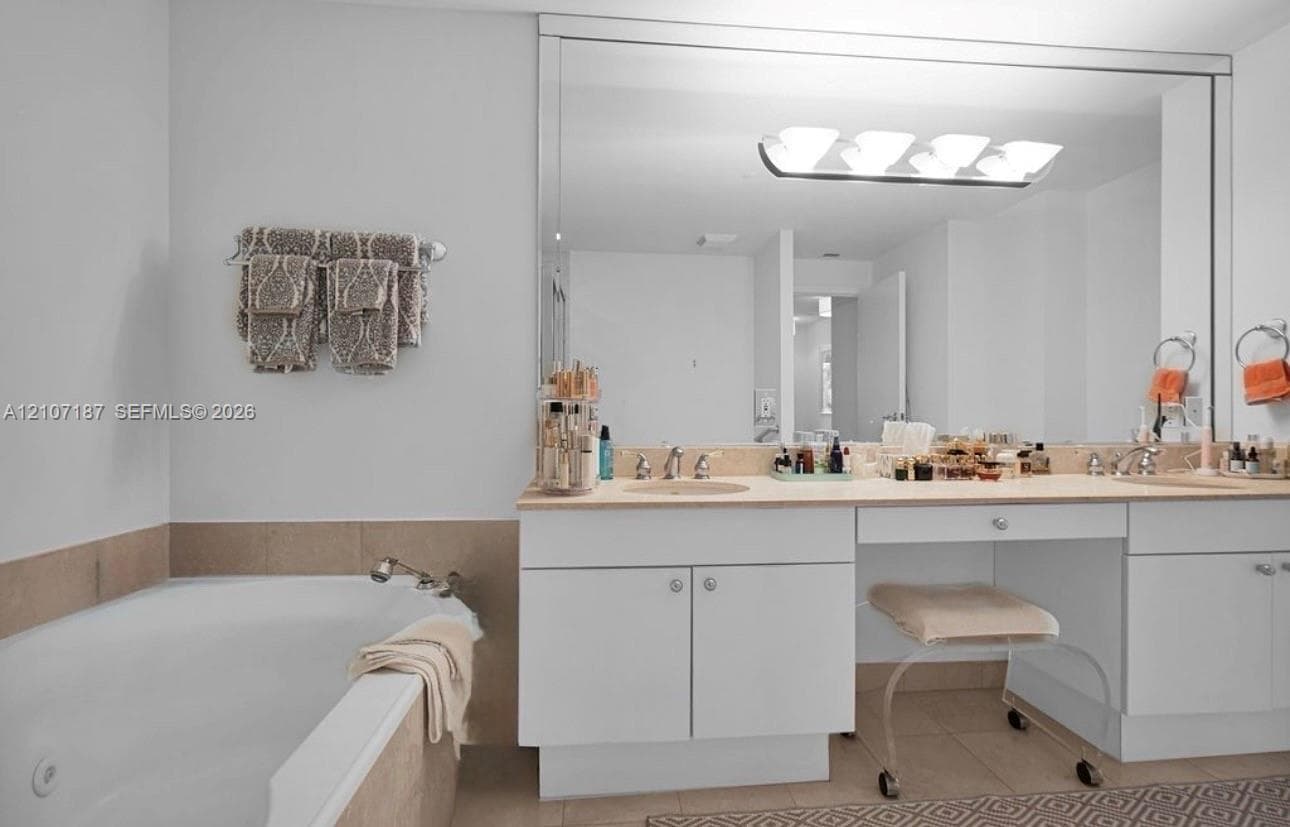 Dual-sink vanity with built-in makeup area, stone countertop, recessed lighting, and integrated full-width mirror, paired with a built-in soaking tub featuring stone tile surround