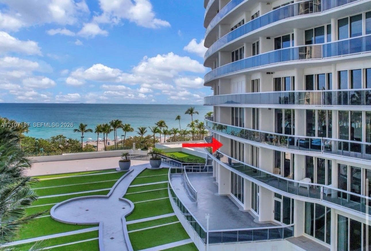 High-rise exterior featuring curved glass-railing balconies, floor-to-ceiling windows, and landscaped grounds with paved walking paths