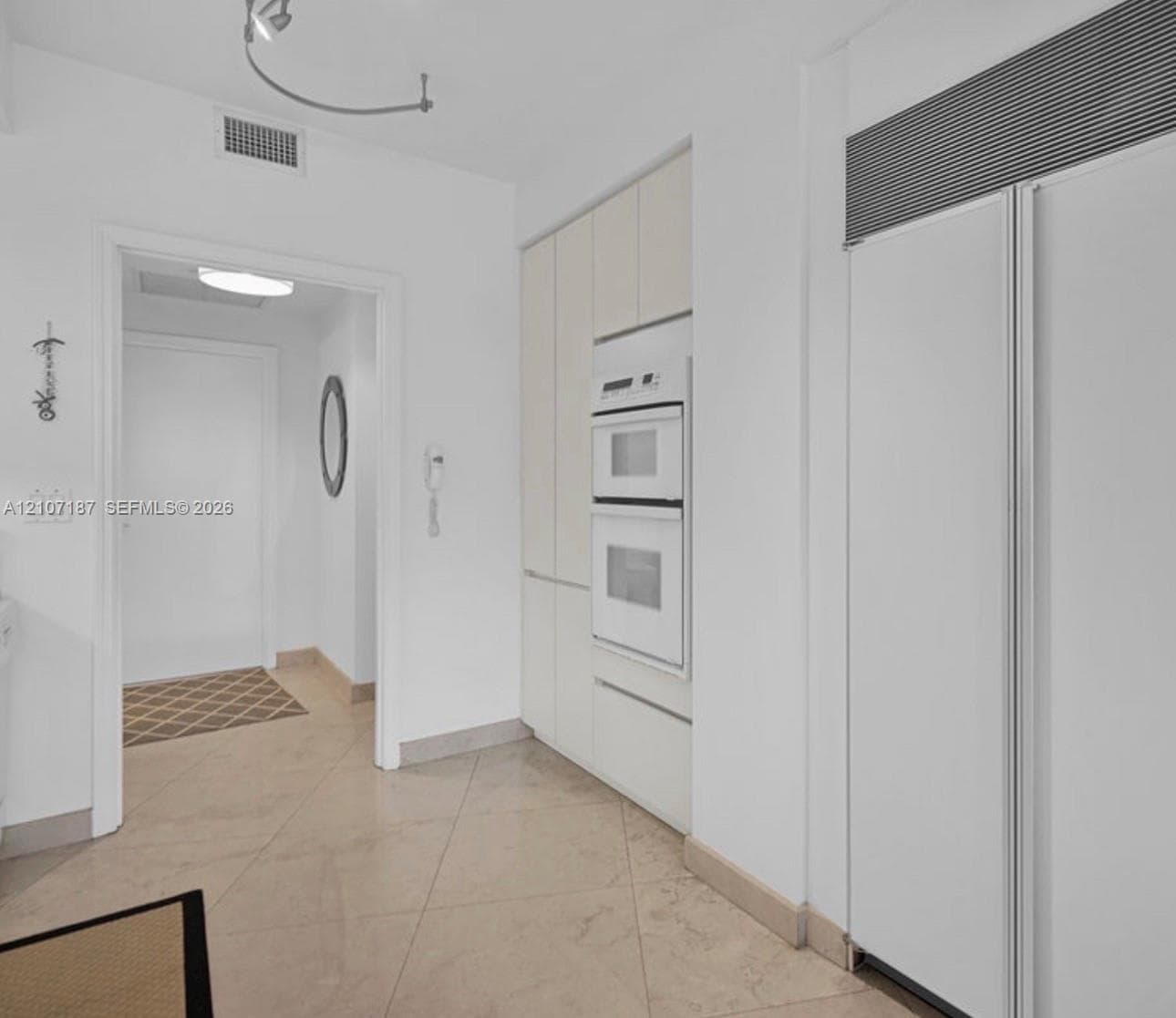 Built-in double wall oven, integrated panel-ready refrigerator, and custom flat-panel cabinetry, complemented by oversized ceramic floor tiling