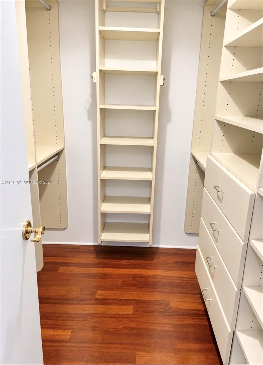 Walk-in closet featuring wood-finish flooring, custom built-in shelving, integrated hanging rods, and a multi-drawer storage unit with metallic hardware