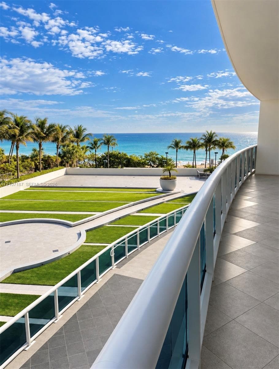 Expansive curved terrace featuring large-format stone tile flooring, a minimalist glass and white metal railing, and direct sightlines to the coastline and ocean
