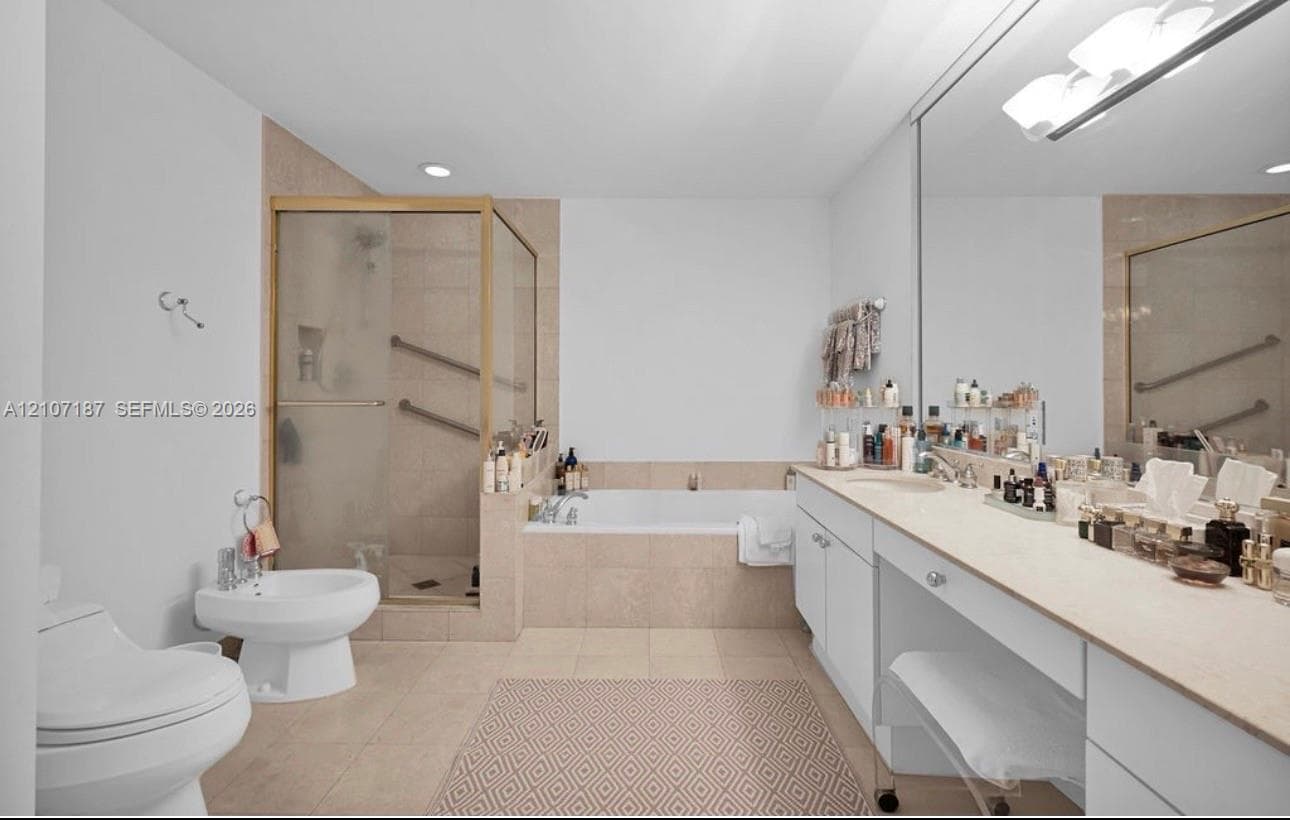 Bathroom featuring a dual-sink vanity with light-toned countertops, a glass-enclosed shower, a separate soaking tub with tiled surround, and a bidet