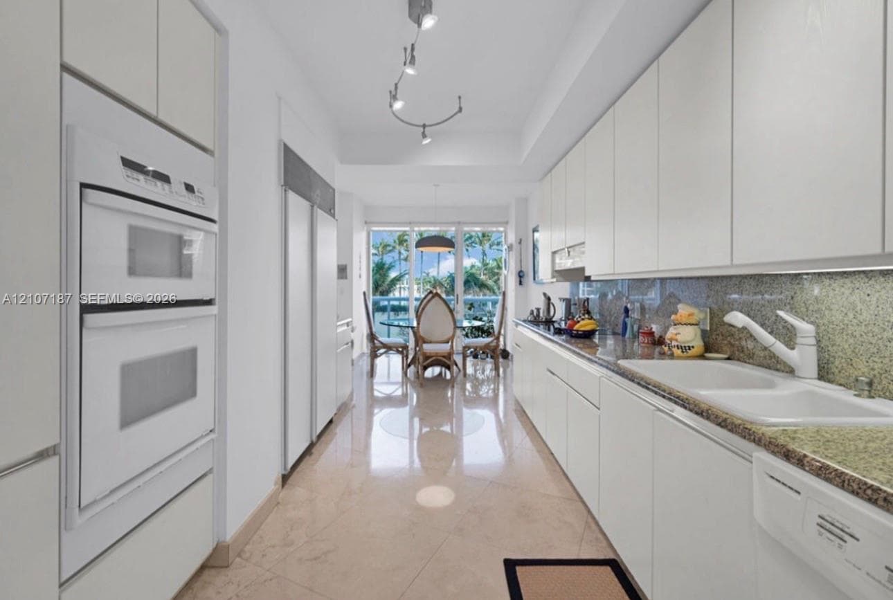 Galley kitchen featuring flat-panel cabinetry, stone countertops, double wall ovens, a dual-basin sink, and polished tile flooring