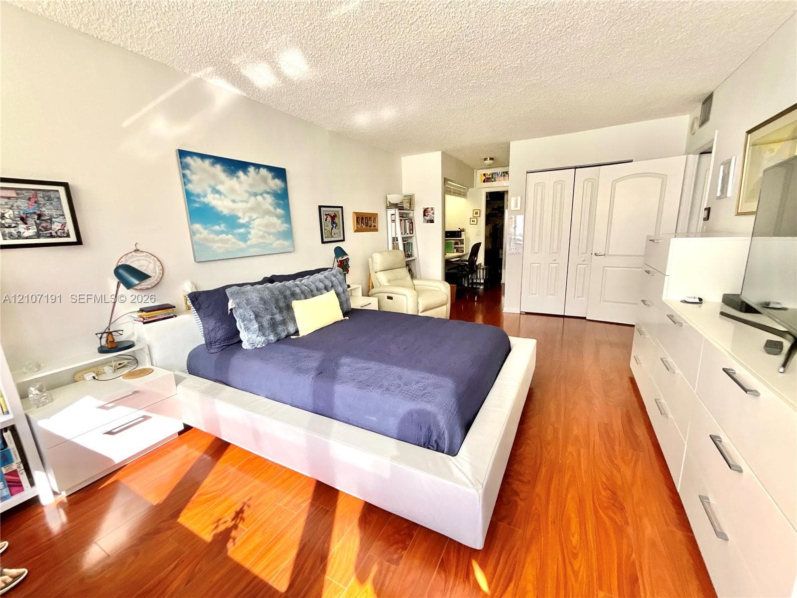 Interior space featuring wood-finish flooring, ceiling with textured finish, and multi-panel closet doors with arched detailing