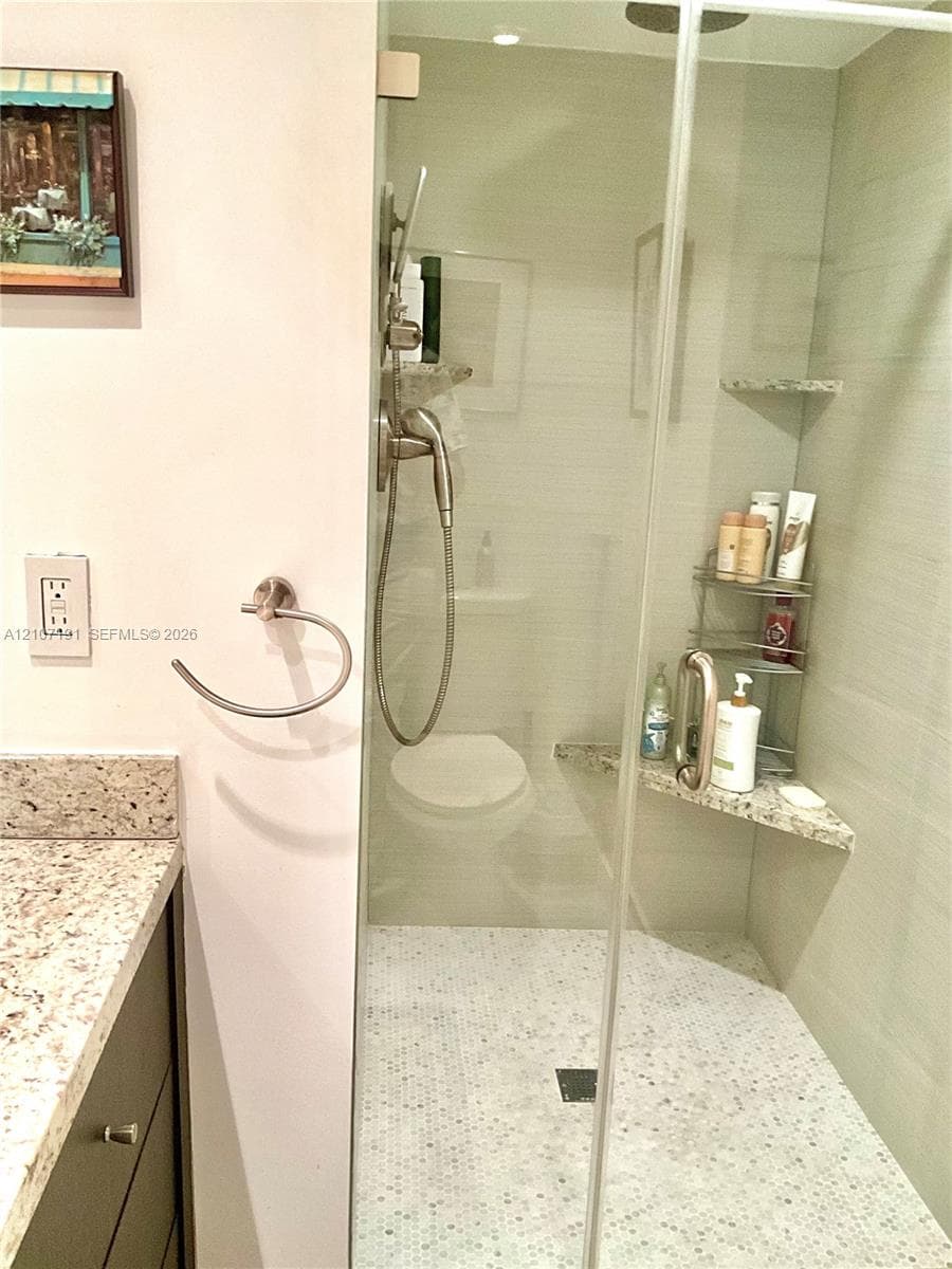 Walk-in shower featuring a frameless glass door, stone tile surround, integrated corner bench, and small-format hexagonal floor tile, complemented by a vanity with a stone countertop