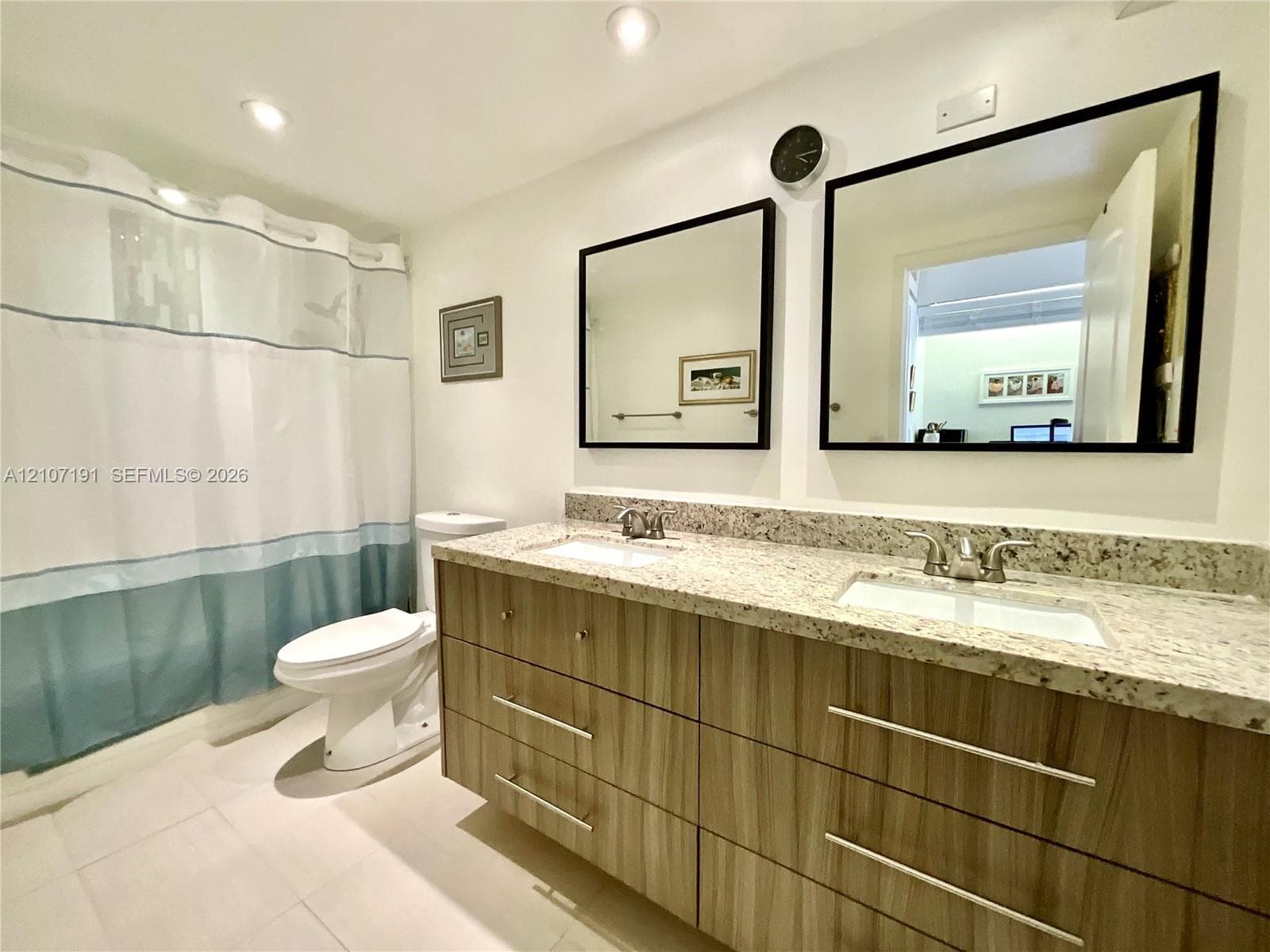 Dual-sink vanity with wood-finish cabinetry, stone countertop, two framed mirrors, and recessed lighting