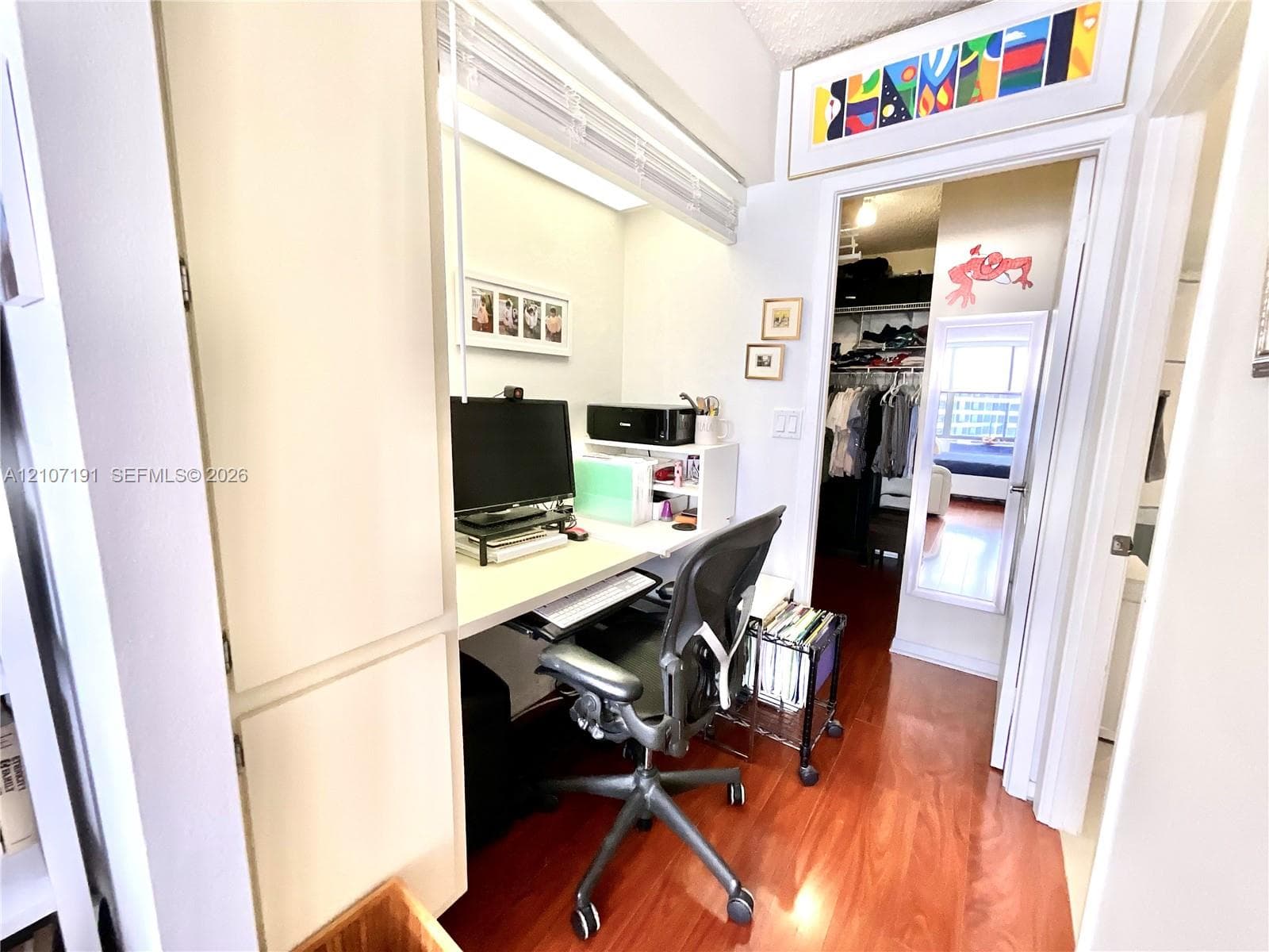 Built-in desk area with overhead lighting and integrated cabinetry, featuring wood-finish flooring and an attached walk-in closet