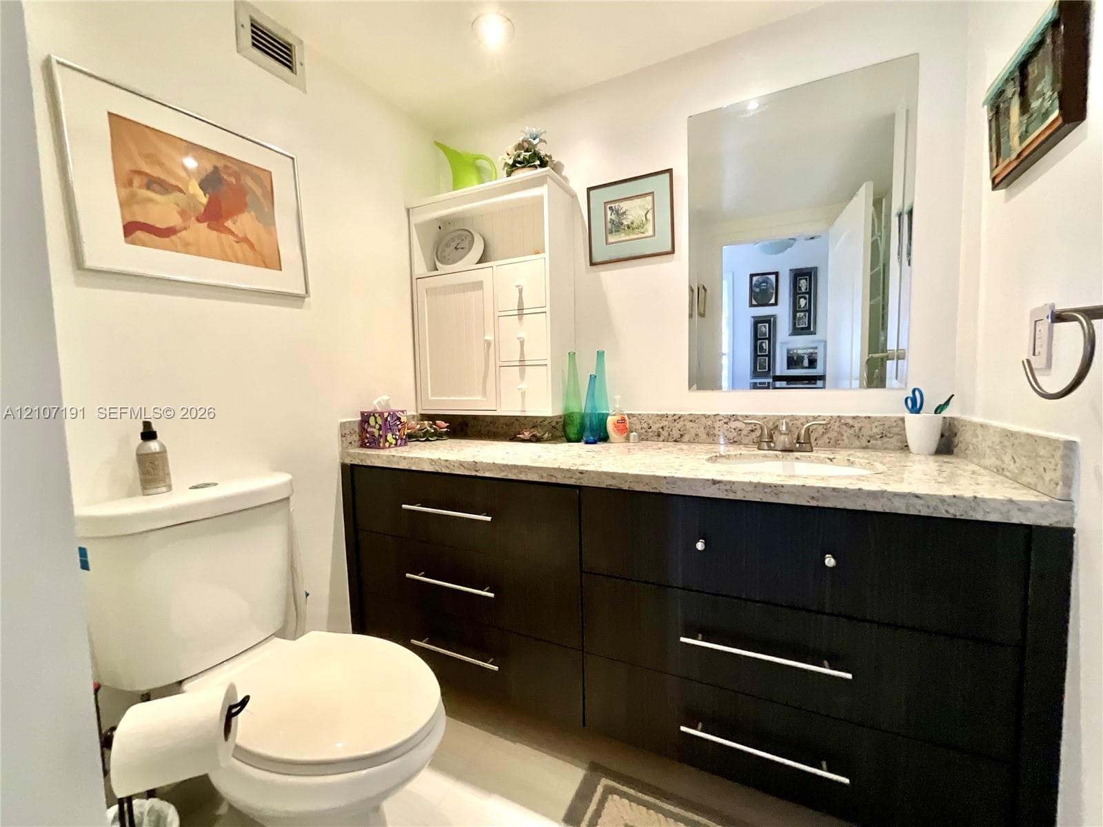 Dark-toned vanity with integrated cabinetry, speckled stone-finish countertop, undermount sink, and recessed wall-mounted mirror