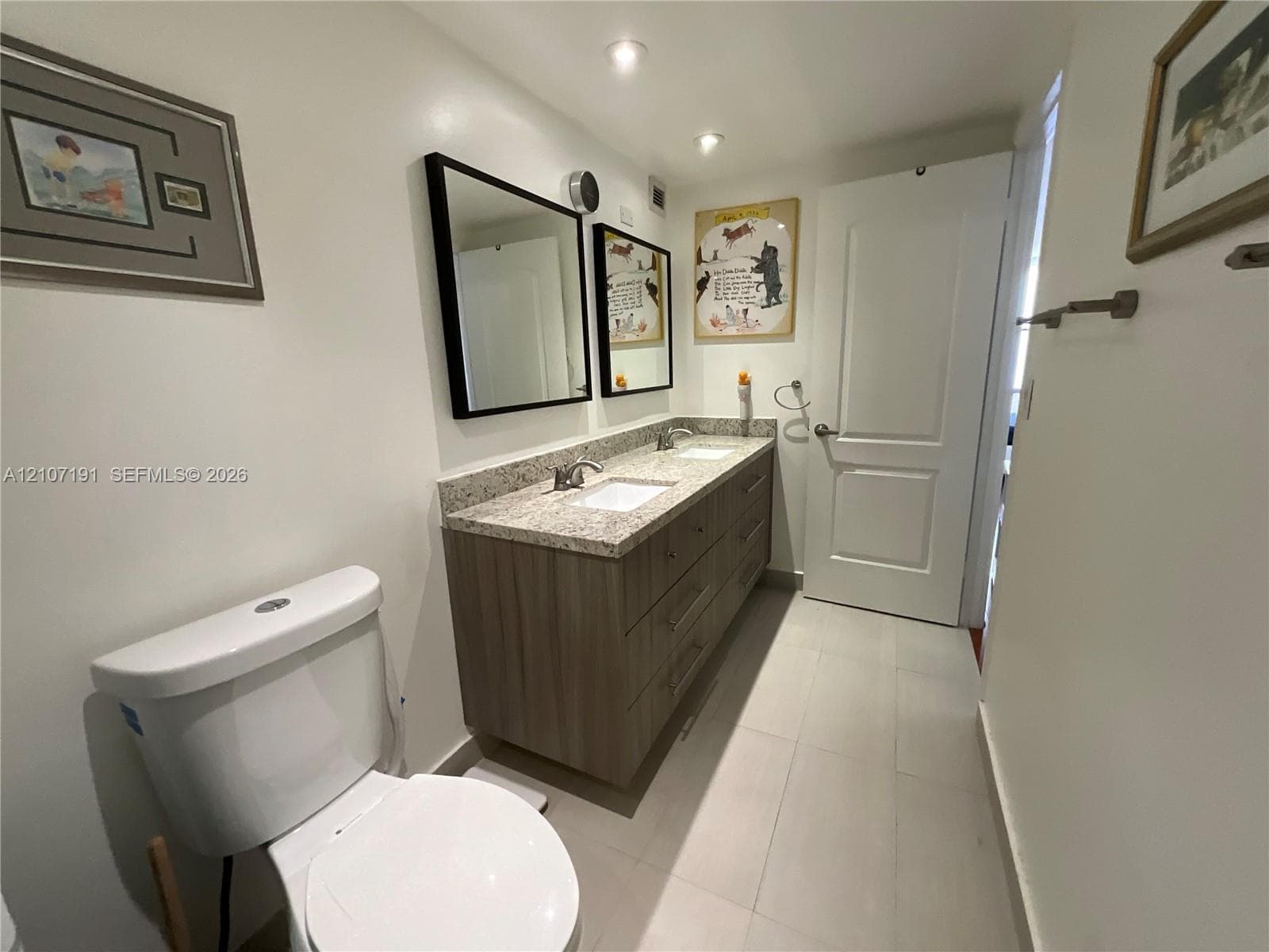 Dual-sink vanity featuring stone-finish countertops, wood-finish cabinetry, rectangular under-mount basins, and two framed wall mirrors