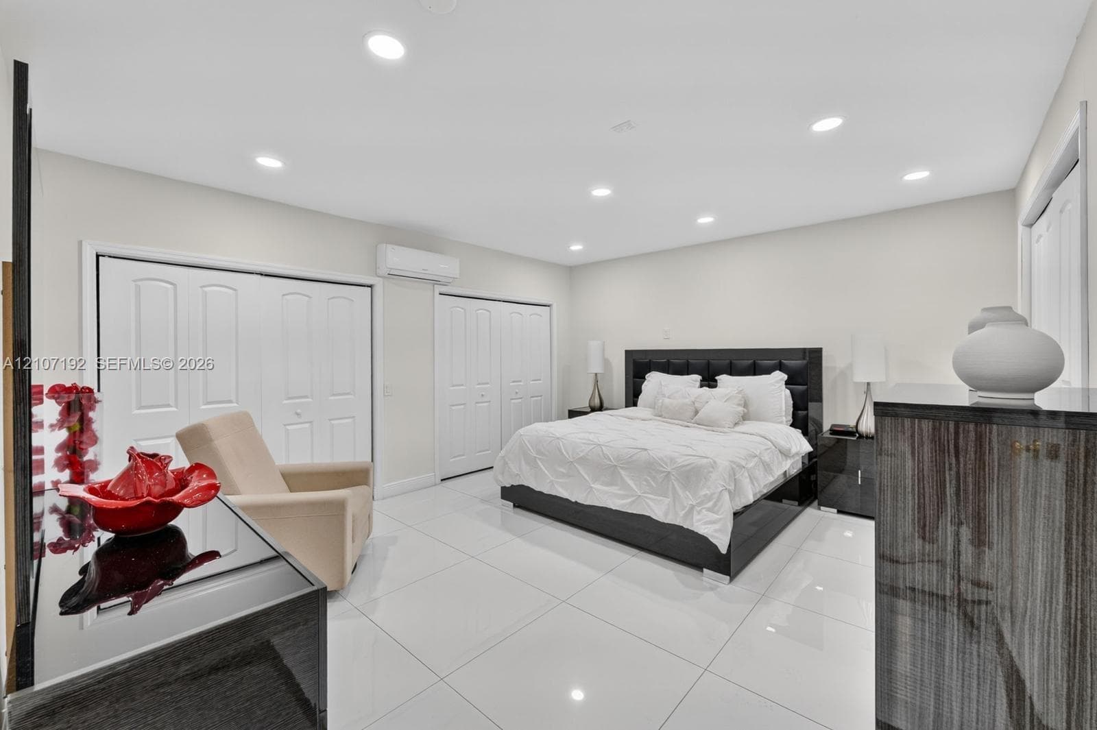 Neutral-toned interior featuring large-format tile flooring, recessed ceiling lighting, dual bi-fold closets, and a wall-mounted climate control unit