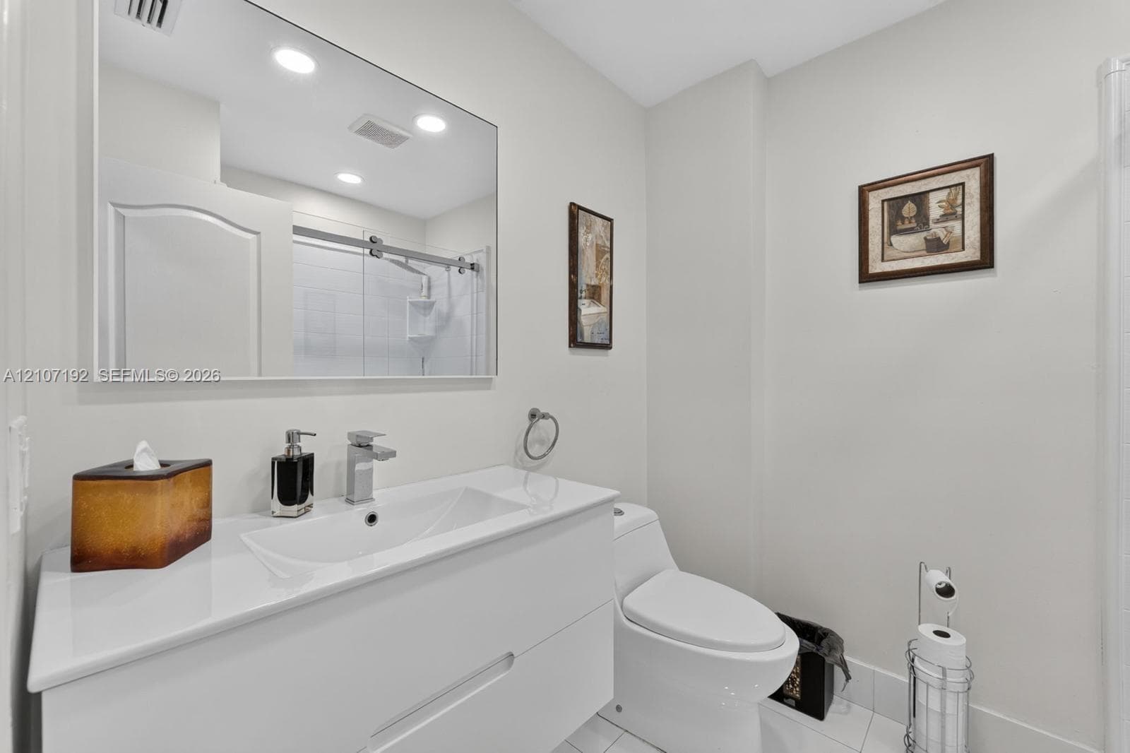 Bathroom featuring a white floating vanity with an integrated countertop sink, chrome faucet, large rectangular wall-mounted mirror, and a glass-enclosed shower