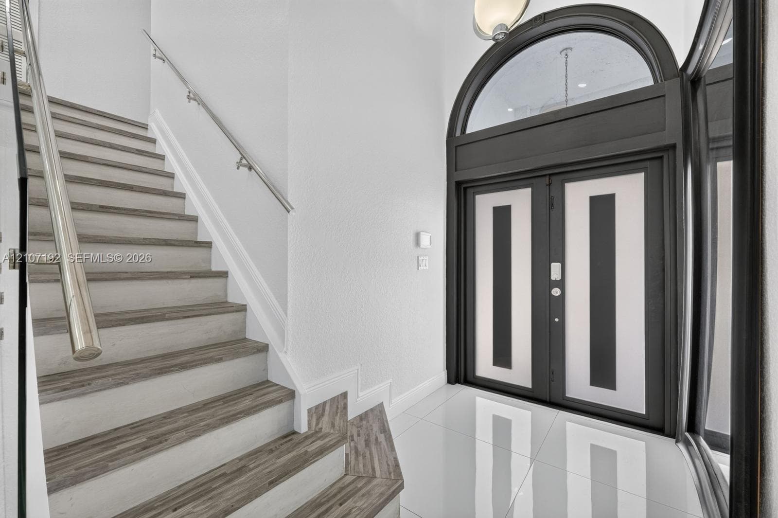Double-door entryway featuring a decorative arched transom window, staircase with wood-finish treads, and polished tile flooring