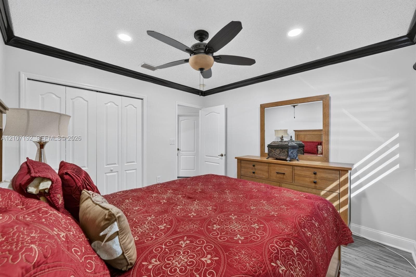 Room featuring wood-finish flooring, dark crown molding, a central ceiling fan with integrated lighting, recessed lighting, and multi-panel doors