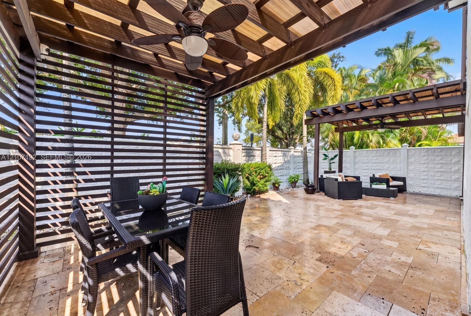 Outdoor patio featuring natural stone pavers, dual wood-slat pergolas, and a ceiling-mounted fan