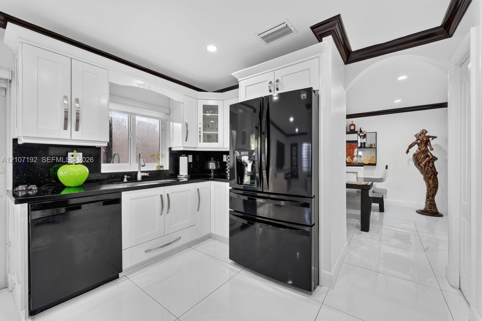 Kitchen featuring white shaker-style cabinetry, black stone countertops, high-contrast black appliances, crown molding, and polished tile flooring