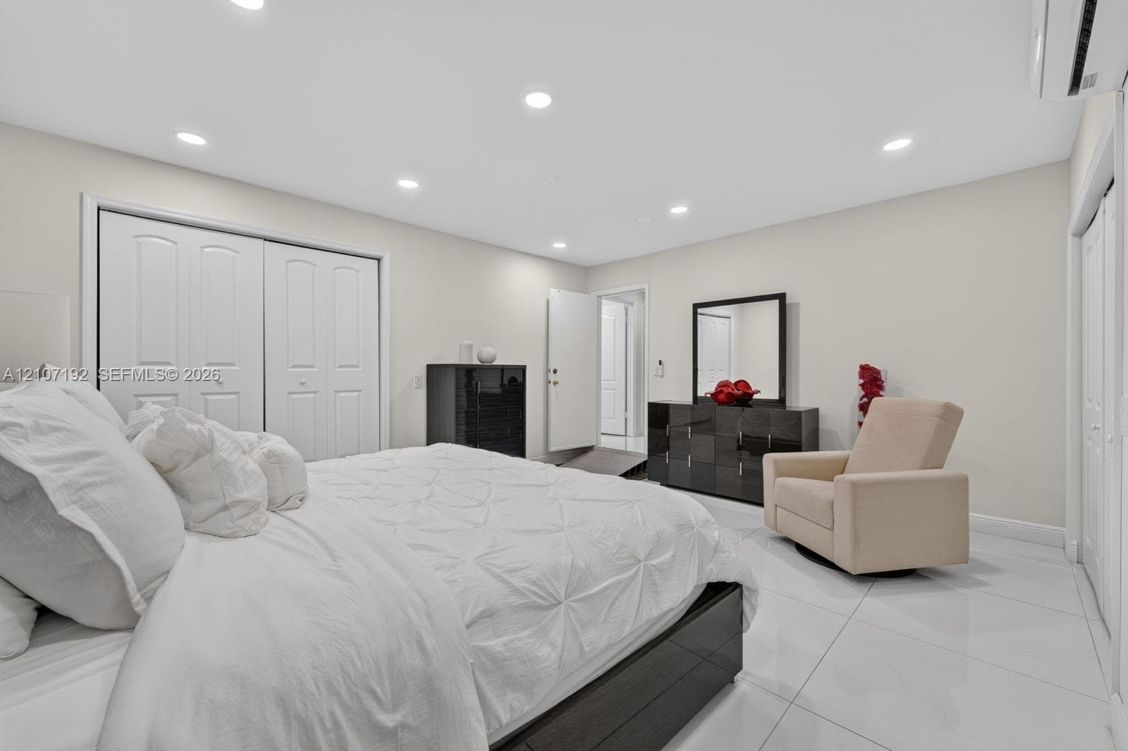 Large-format tile flooring, recessed ceiling lighting, dual sliding-panel closets, and a wall-mounted ductless climate control unit