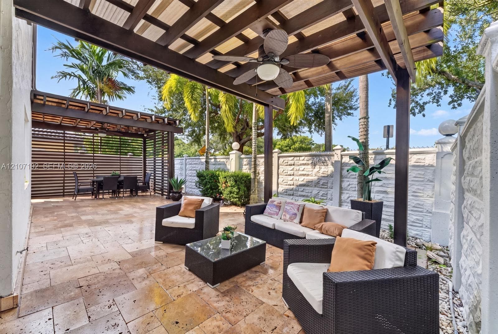 Covered patio featuring a wood-beam pergola, natural stone-finish flooring, a ceiling-mounted fan, and a decorative concrete masonry perimeter wall