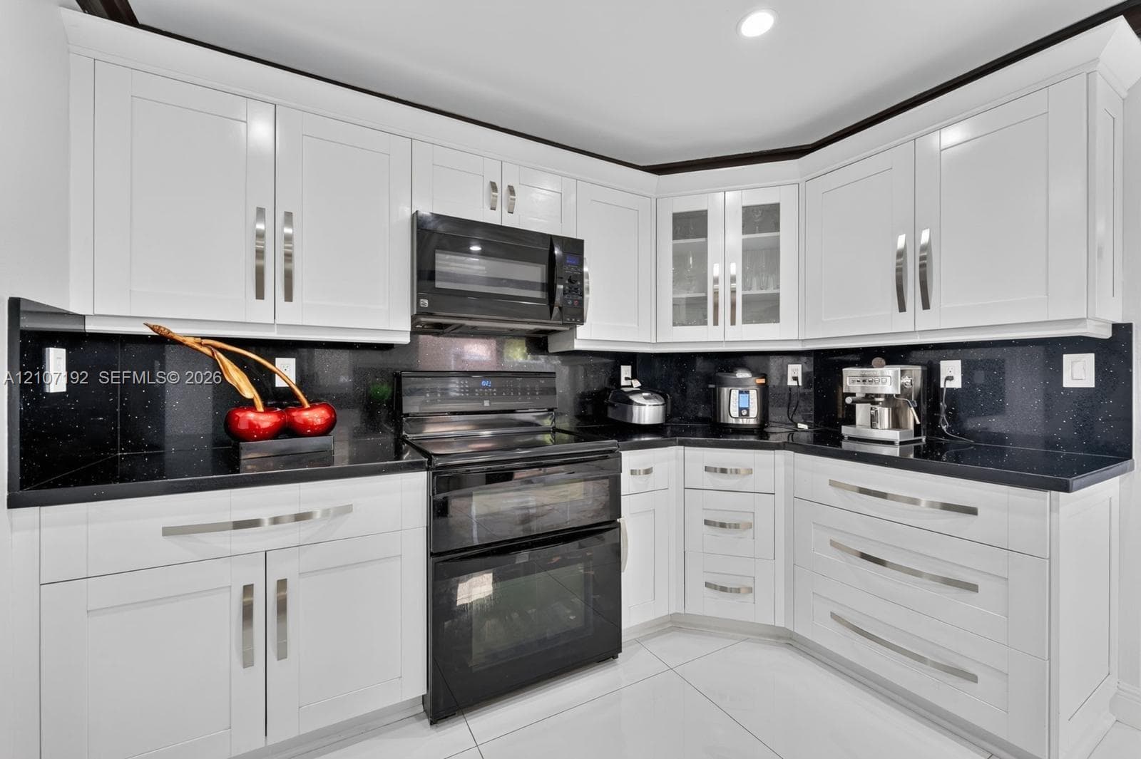 Kitchen featuring white shaker-style cabinetry, black stone countertops, integrated glass-front display cabinets, and recessed ceiling lighting
