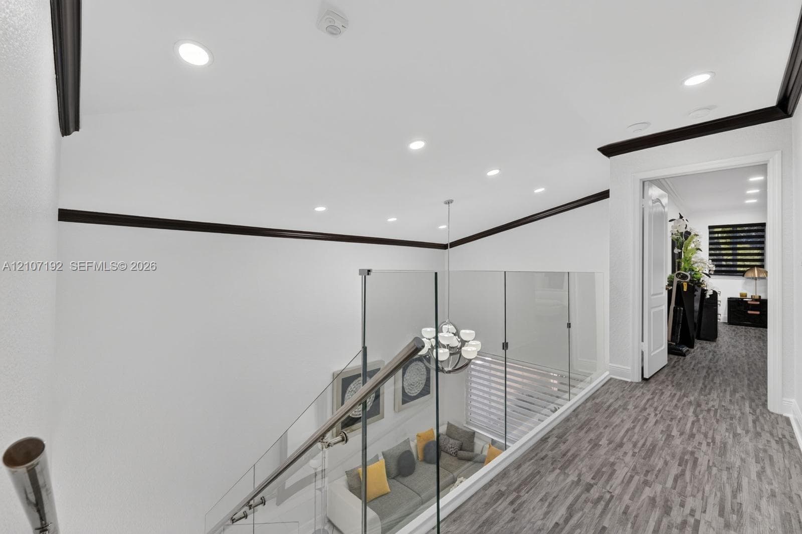 Interior landing featuring wood-finish flooring, glass panel railing with a metallic handrail, recessed ceiling lighting, and dark-toned crown molding