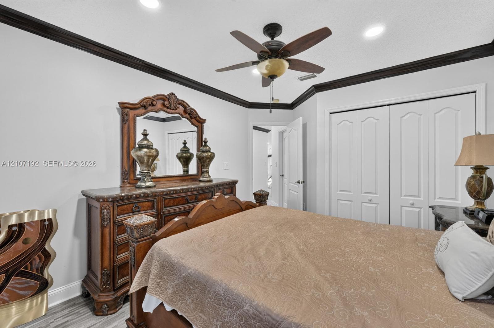 Room featuring high-contrast dark crown molding, wood-finish flooring, recessed lighting, a ceiling fan with integrated lighting, and white bi-fold closet doors