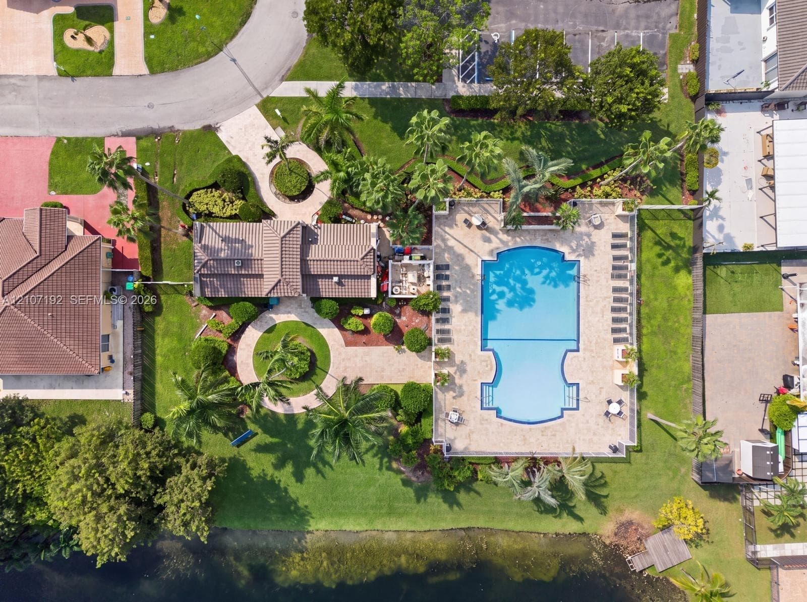 Aerial perspective featuring a sprawling property with a custom-shaped swimming pool, extensive paver hardscaping, mature palm landscaping, and direct waterfront access