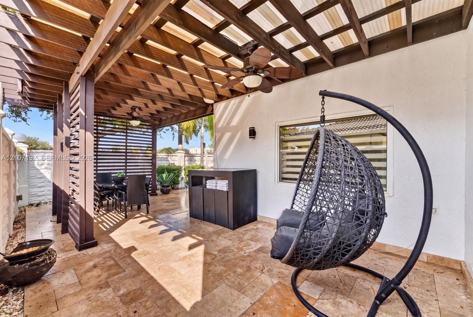 Covered patio featuring natural stone tile flooring, a custom wood pergola, dual ceiling fans, and a slatted privacy screen