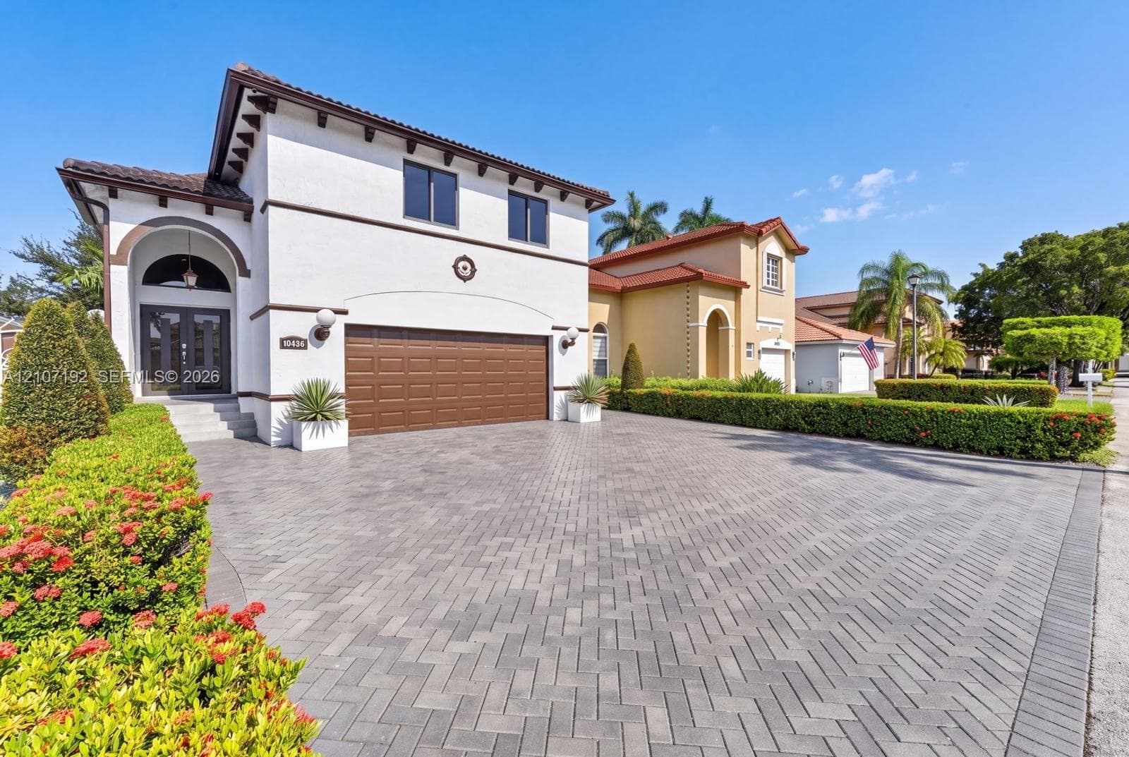 Stucco exterior featuring arched architectural detailing, a multi-car garage, and a herringbone-patterned paver driveway