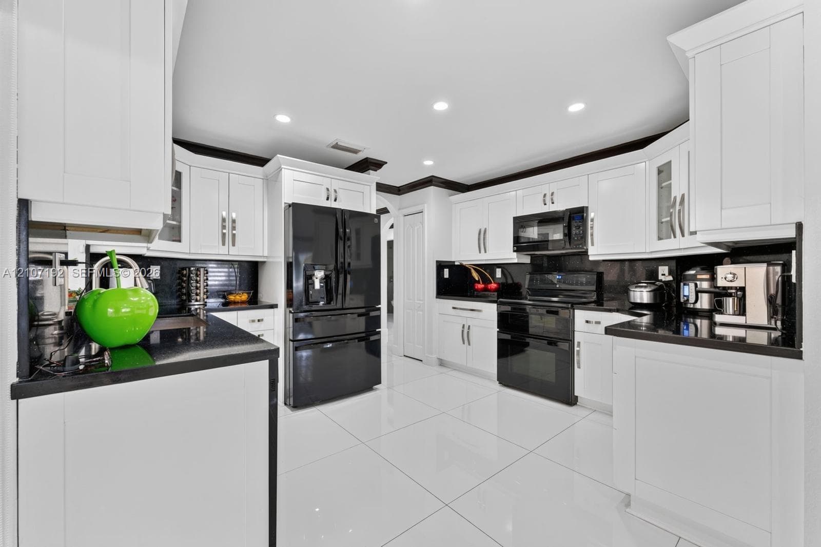 Kitchen featuring white shaker-style cabinetry, high-contrast black countertops, polished tile flooring, recessed lighting, and built-in black appliances
