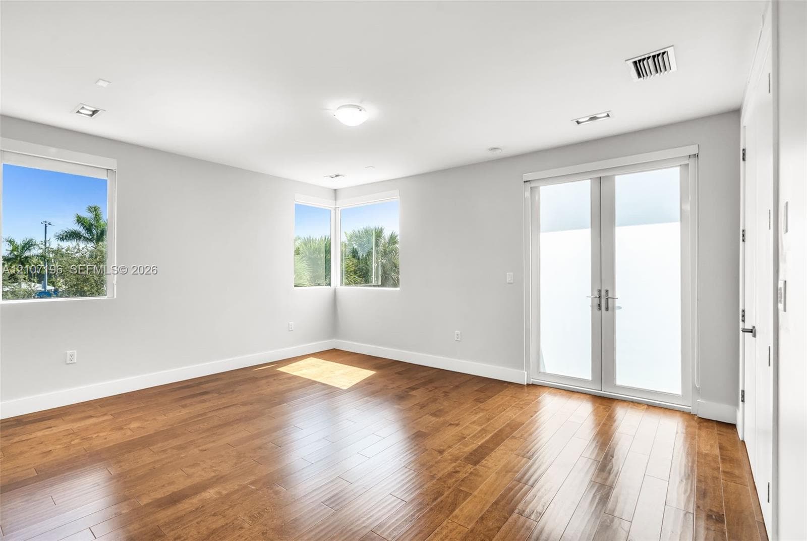 Room featuring wood-finish flooring, recessed lighting, double French doors, and windows with exterior greenery