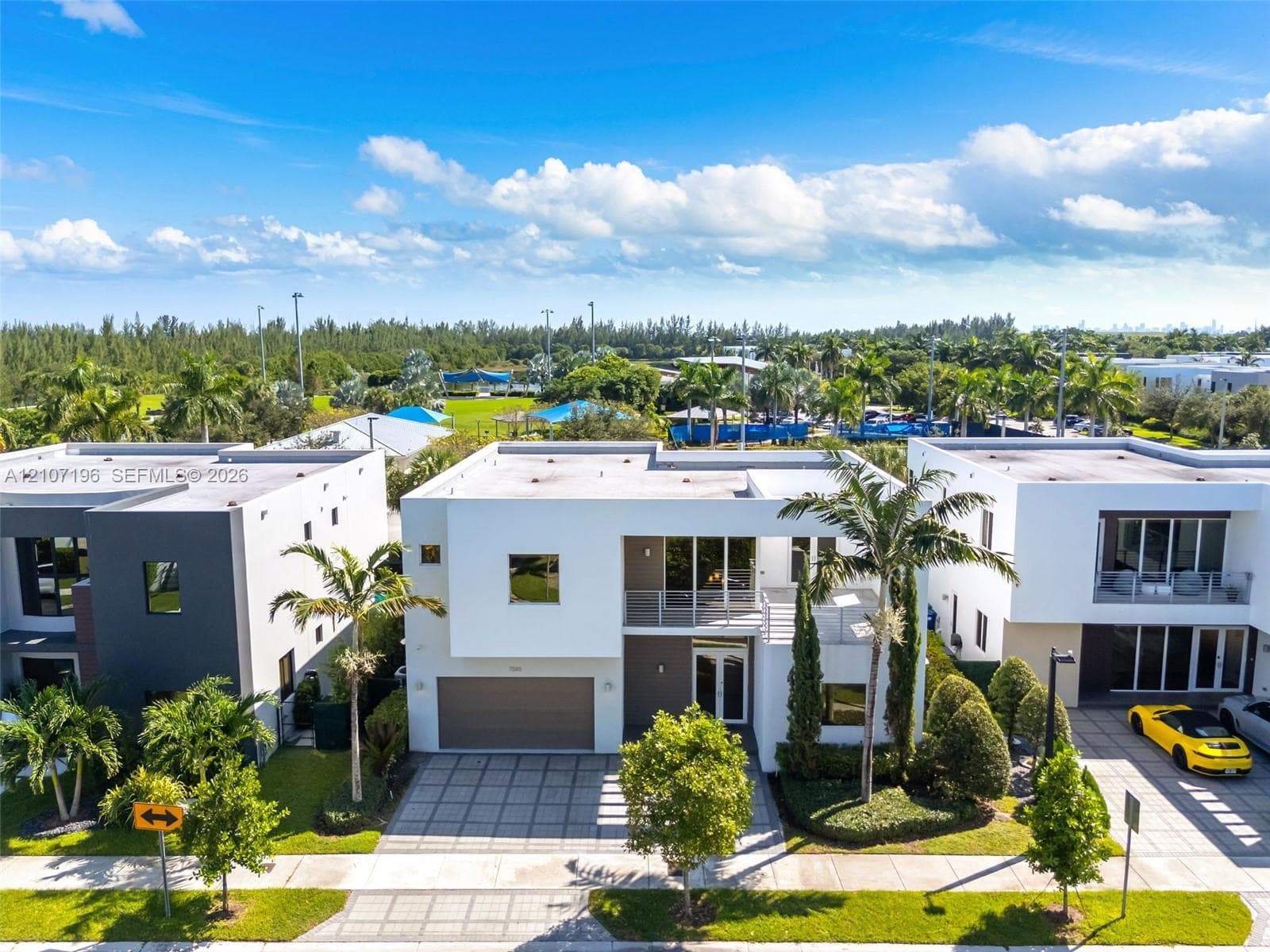 Modern two-story architectural exterior featuring a flat roofline, grid-patterned concrete paver driveway, attached two-car garage, second-level balcony with metal railing, and expansive glass window wall