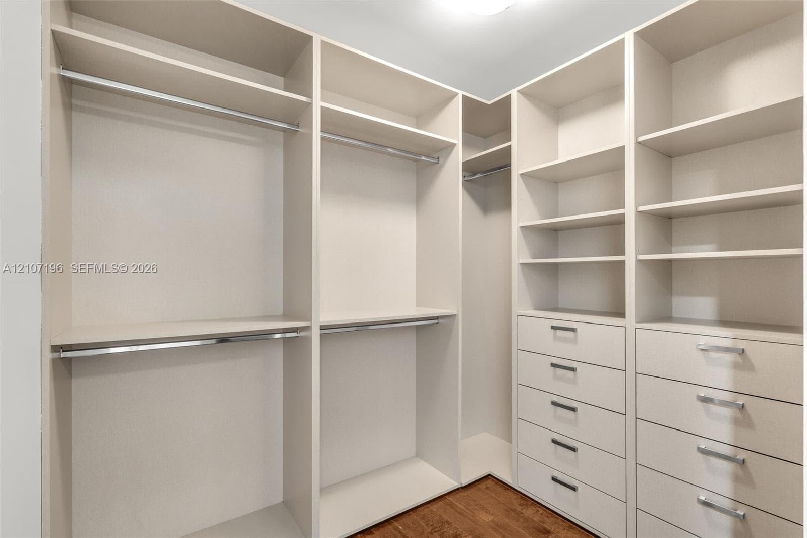 Custom walk-in storage featuring floor-to-ceiling shelving, integrated stainless steel hanging rods, and multiple soft-close drawers with metallic pulls, complemented by wood-finish flooring