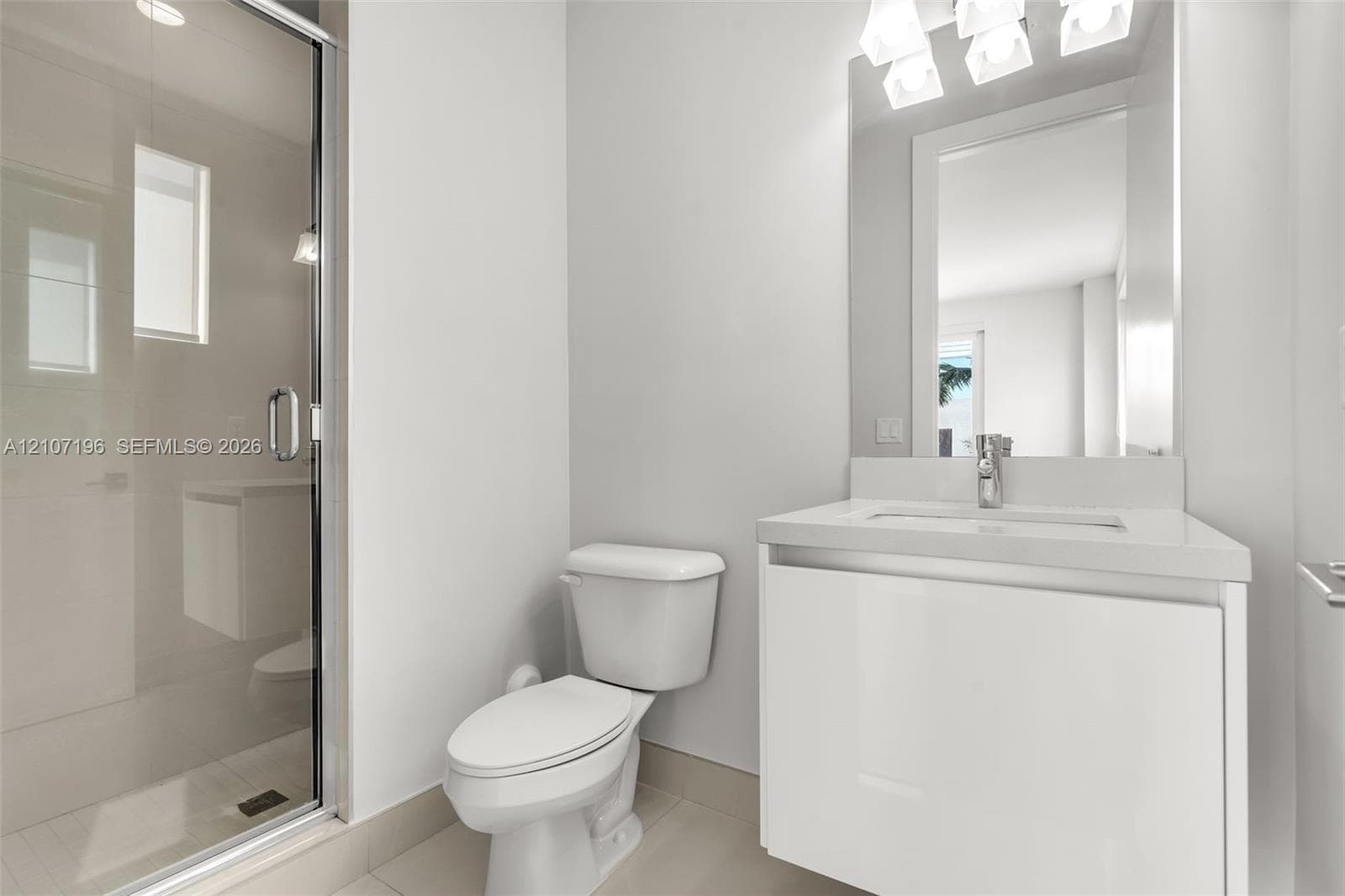 Bathroom featuring a modern floating vanity with a neutral-toned countertop, a glass-enclosed shower with tiled flooring, and a wall-mounted light fixture above the mirror